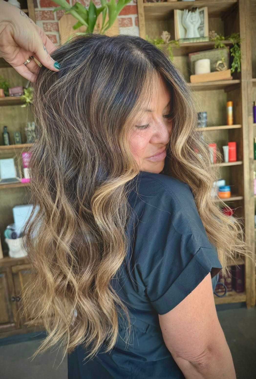 Wavy, highlighted hair on woman in black shirt, styled in a salon setting.