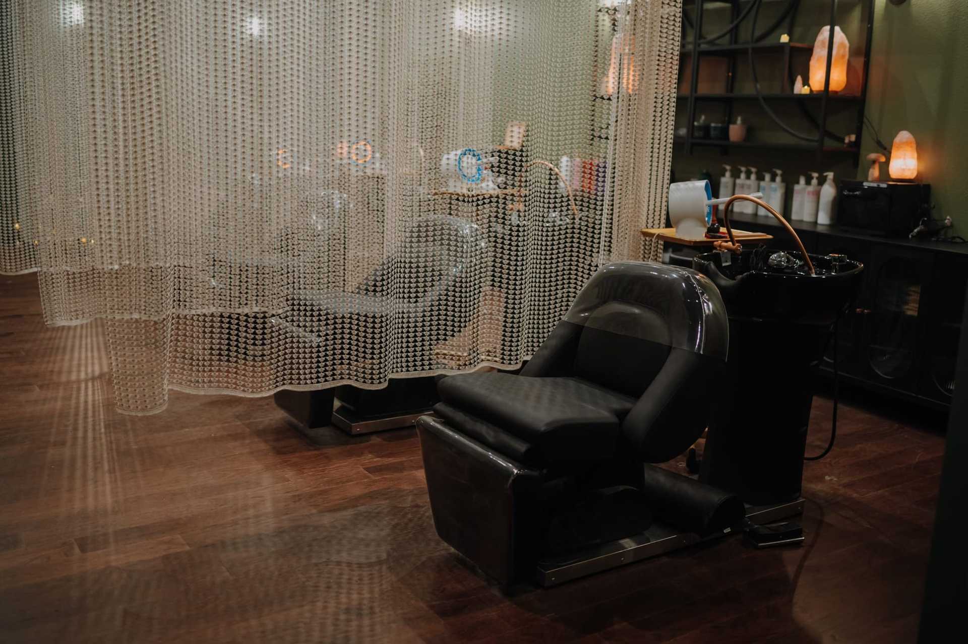 Salon hair washing station with black chairs, chain curtains, and shelves with hair products.