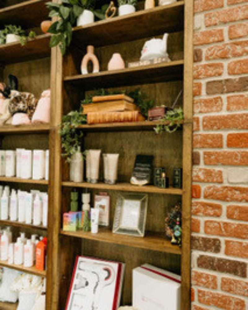 Shelf with books, plants, skincare products, and decorative items against a brick wall.