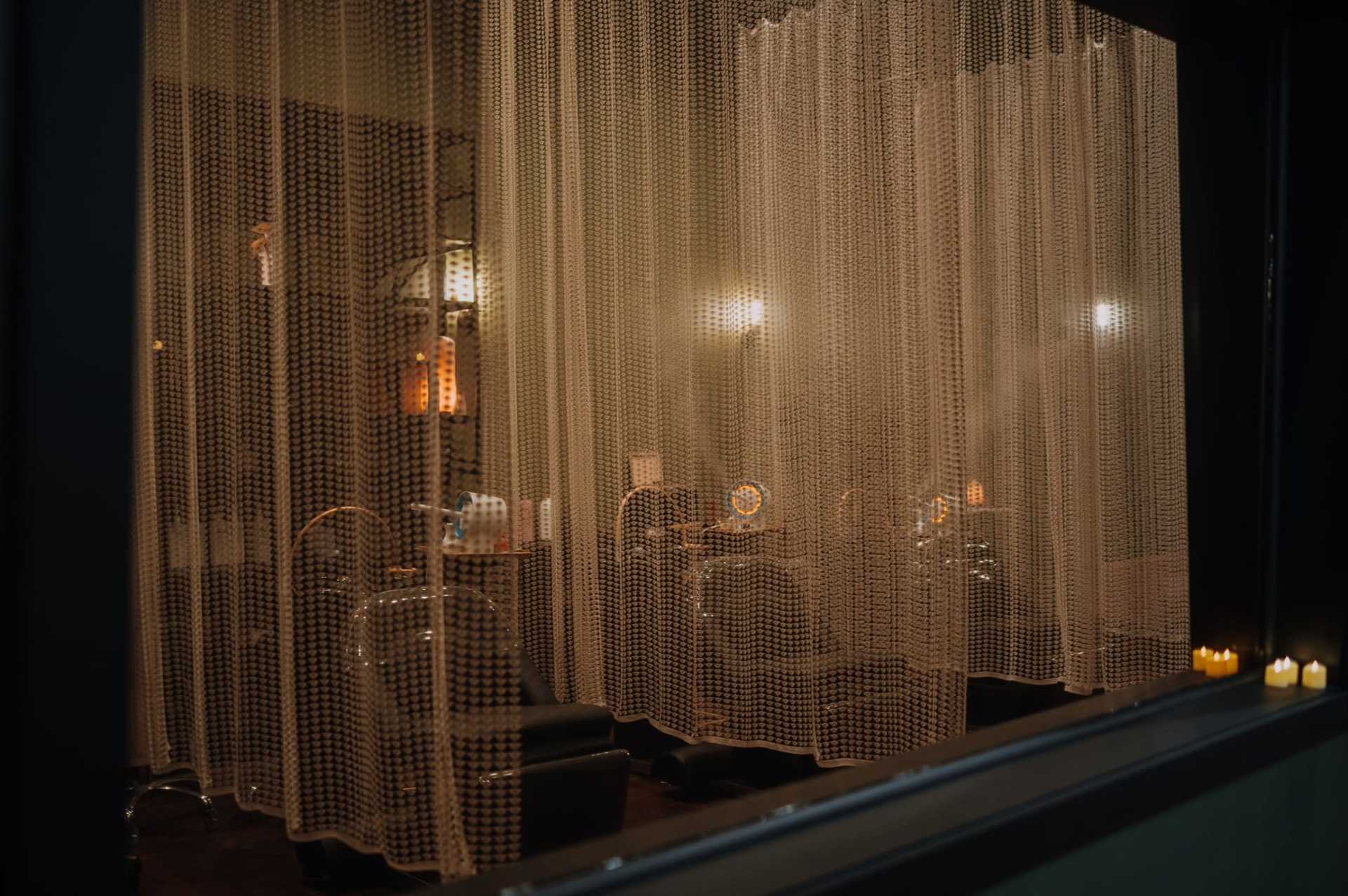 Dimly lit beauty salon behind bead curtains with illuminated vanity mirrors and candles.