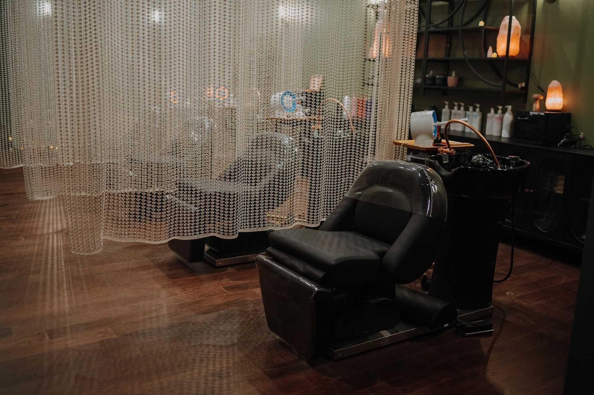 Salon hair washing station with black chairs, chain curtains, and shelves with hair products.