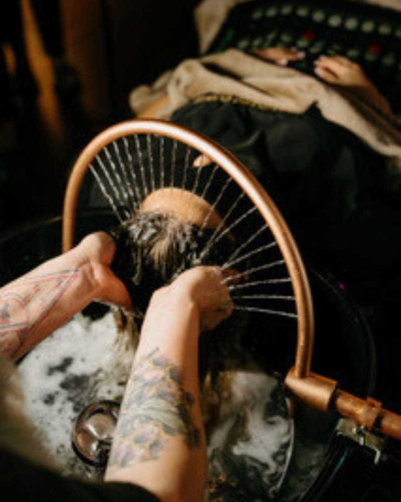 Person gets hair washed in a salon with a copper showerhead.