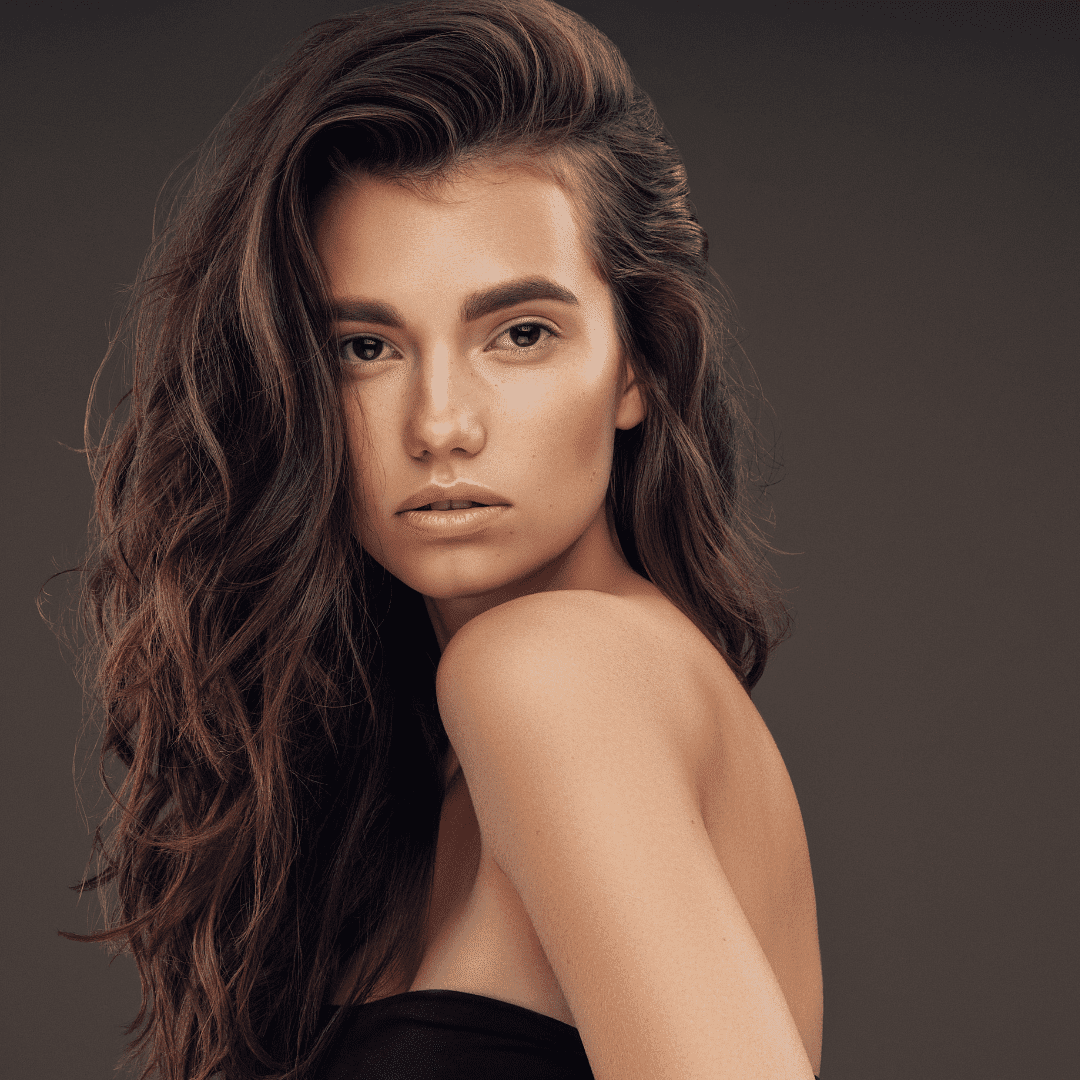 Portrait of a woman with long, wavy hair against a dark background, looking directly at the camera.