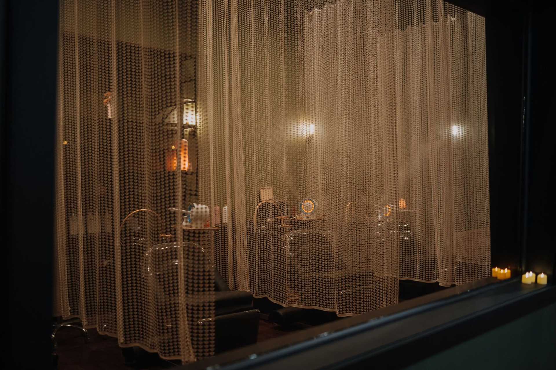 Dimly lit beauty salon behind bead curtains with illuminated vanity mirrors and candles.