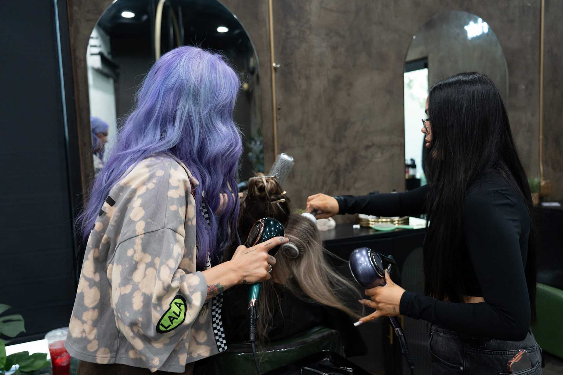 Two hairstylists working on a client's hair in a salon.