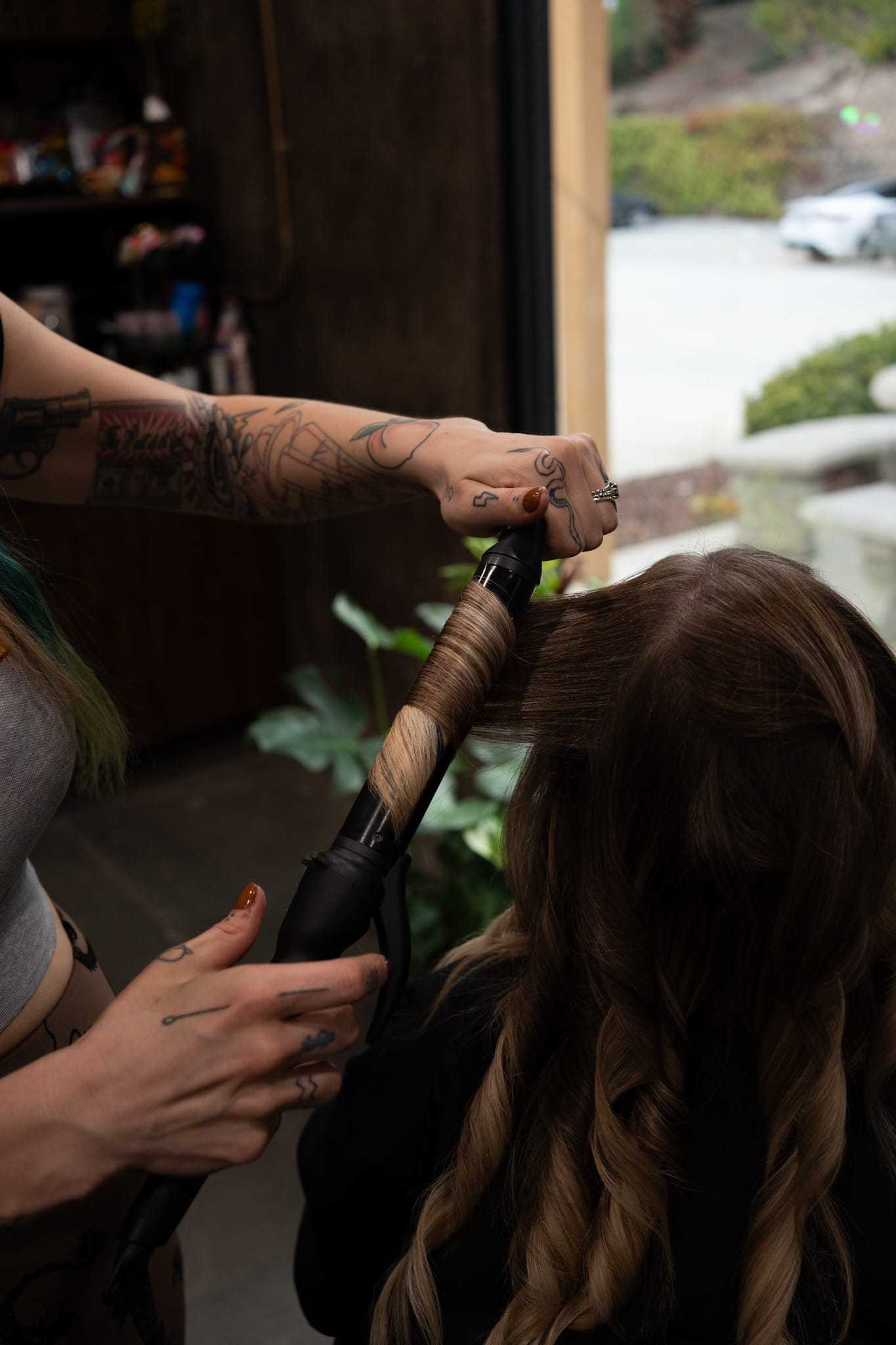 Hairdresser curling a client's hair with a styling wand in a salon setting.