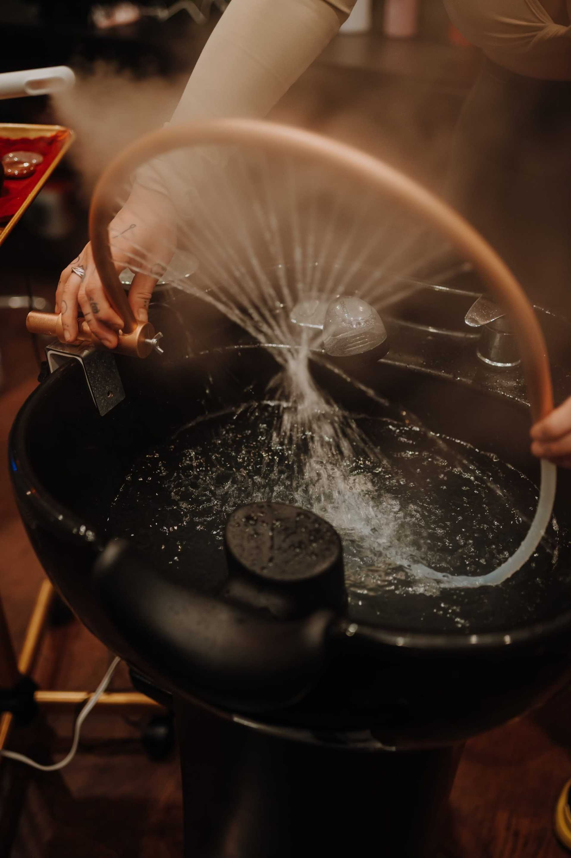 Person rinsing hair at washbasin with a flexible hose in a salon.