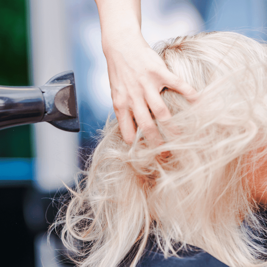 A stylist blow-dries a client's blonde hair.