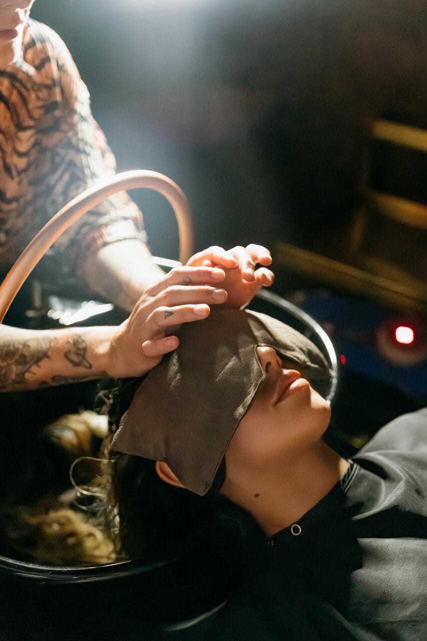 Person receiving a relaxing hair wash at a salon, with a towel over their eyes.
