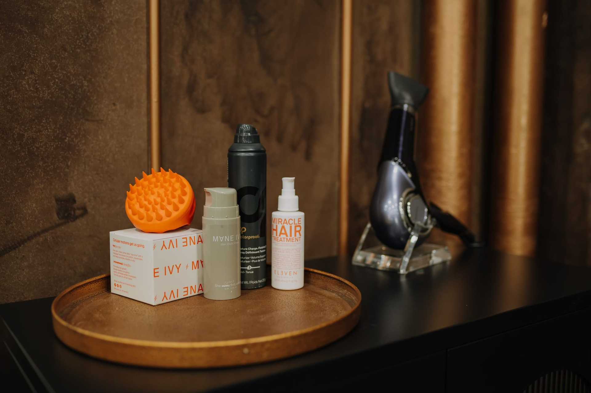 Haircare products including a massager, spray, and treatments on a wooden tray.