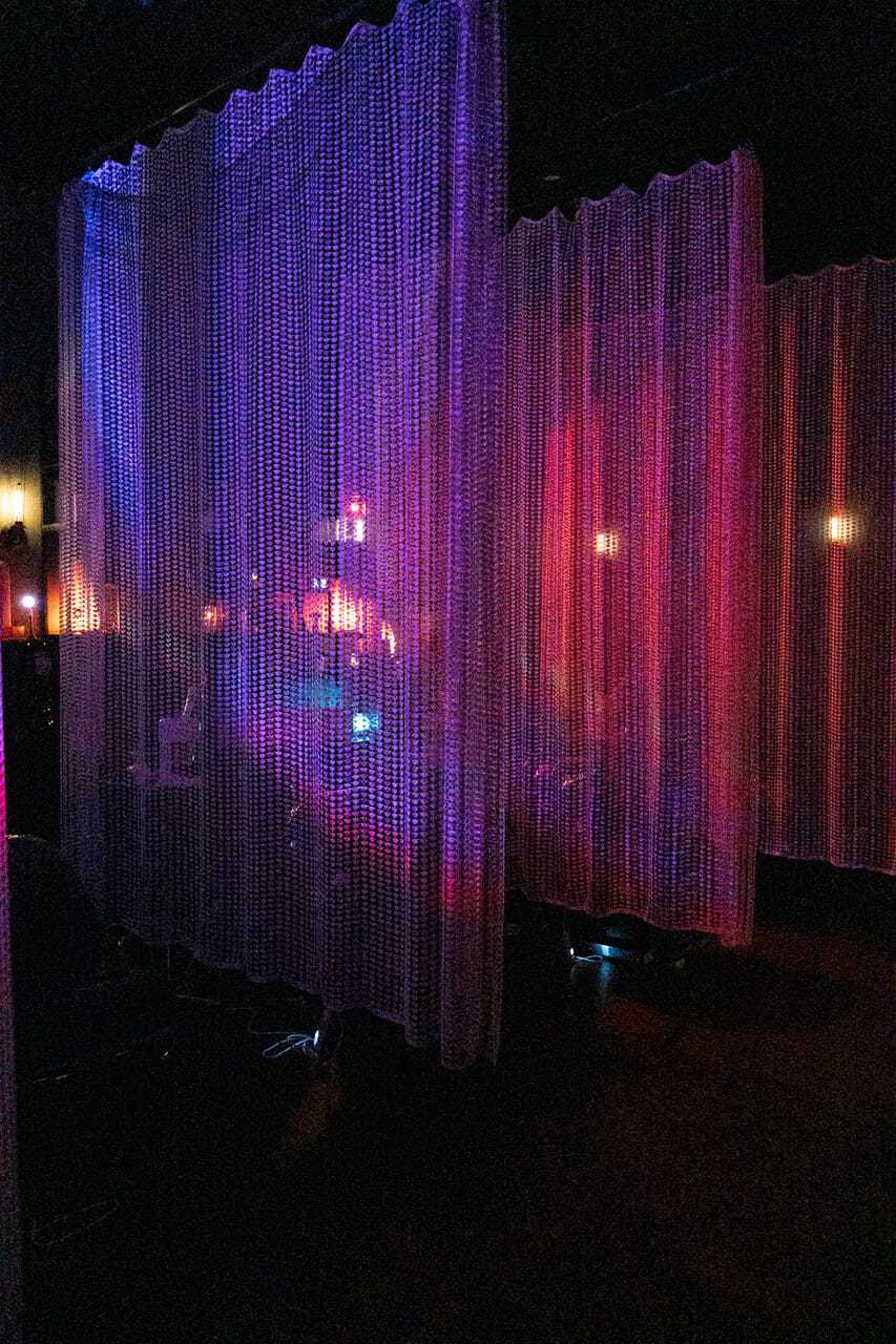 Colorful lights illuminate mesh curtains in a dimly lit room.