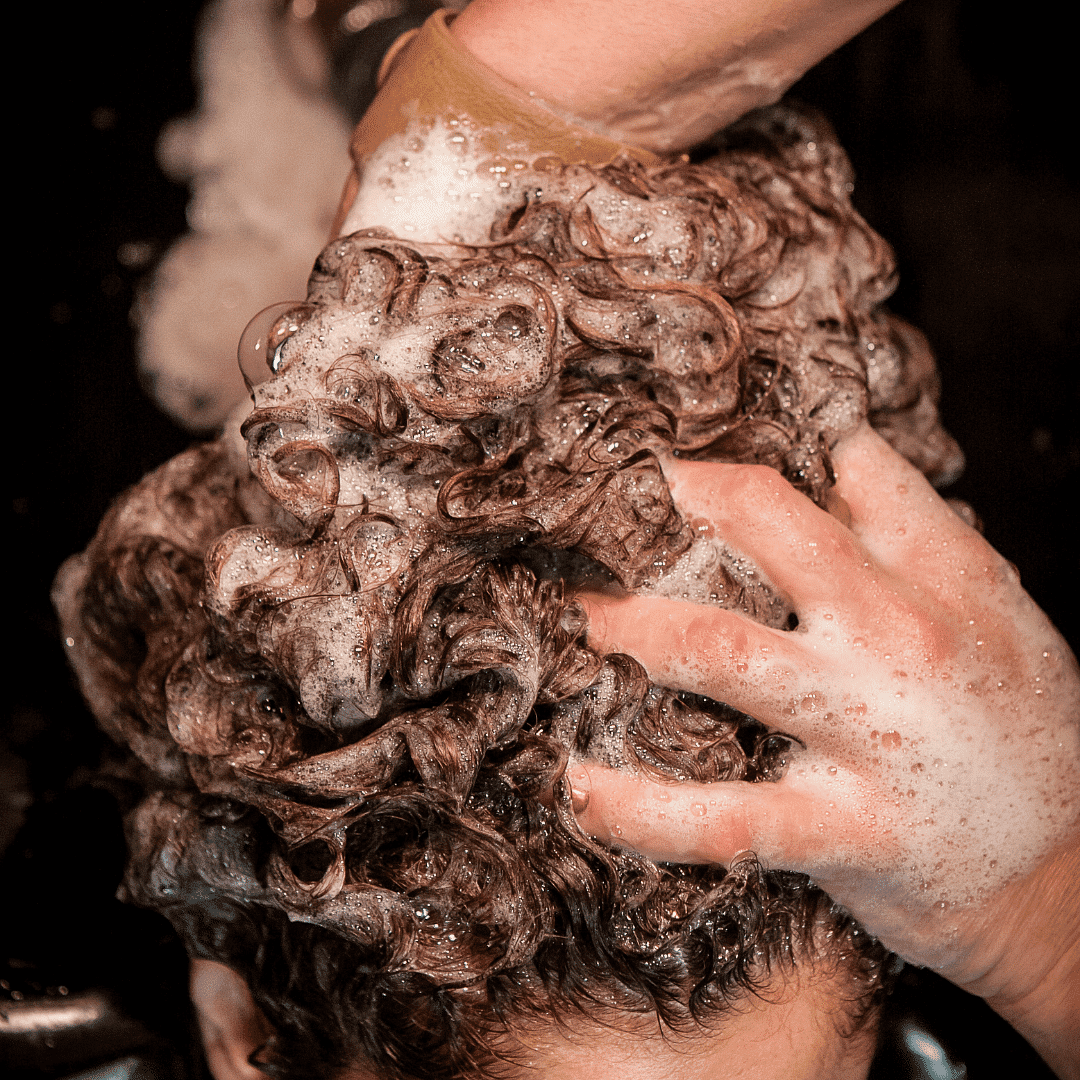 Person washing curly hair with soap, creating foamy lather.